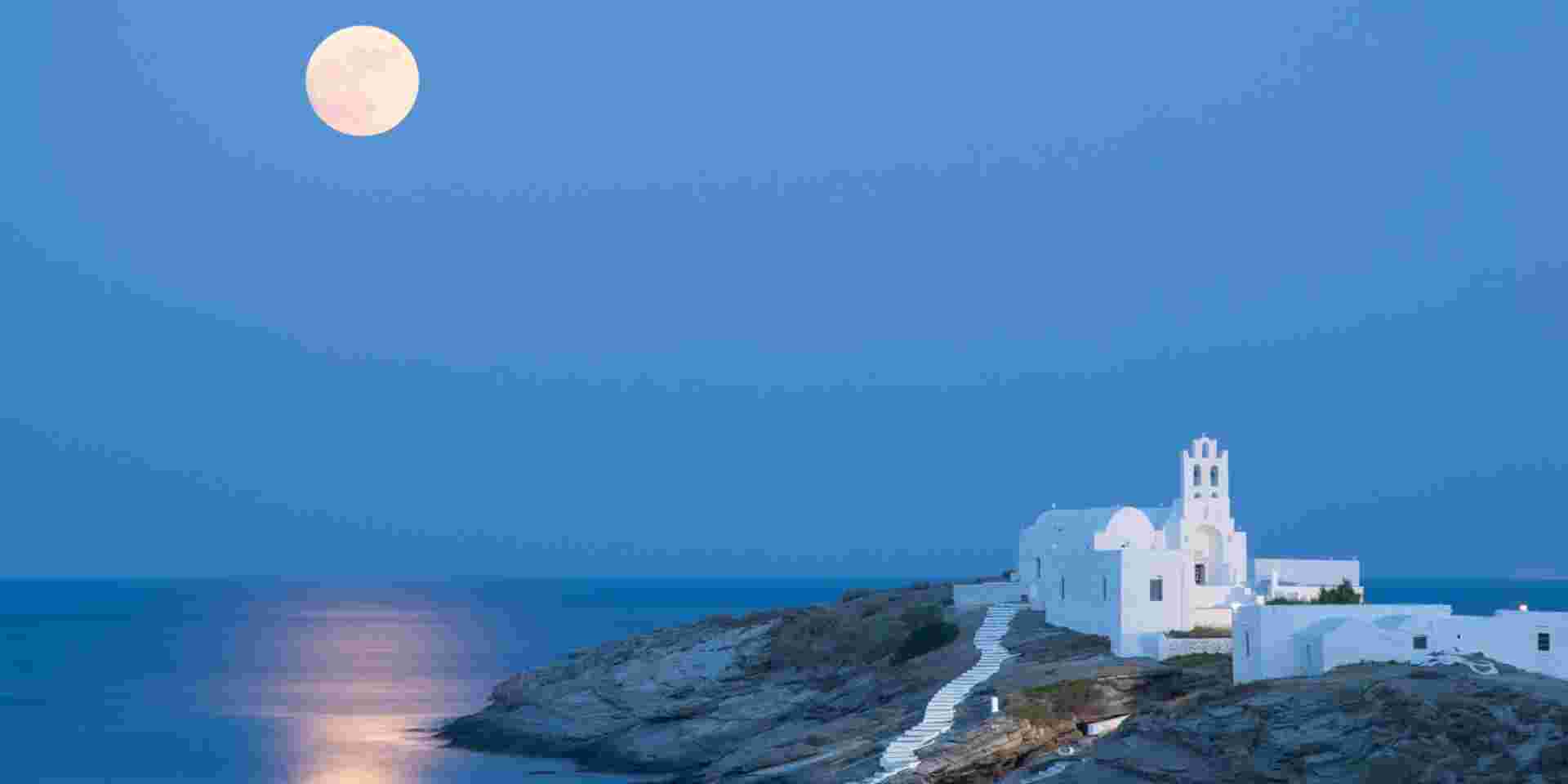 A summer picture of the island Sifnos with the full moon and its reflections on the Aegean Sea. The famous church of Panagia Chrysopigi on the foreground. unique places to visit in greece_feature