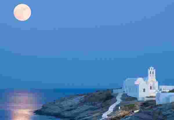 A summer picture of the island Sifnos with the full moon and its reflections on the Aegean Sea. The famous church of Panagia Chrysopigi on the foreground. unique places to visit in greece_feature