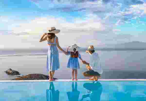 A beautiful family stands at the edge of a swimming pool and enjoys the view over the ocean during their holidays Greece family vacation_feature