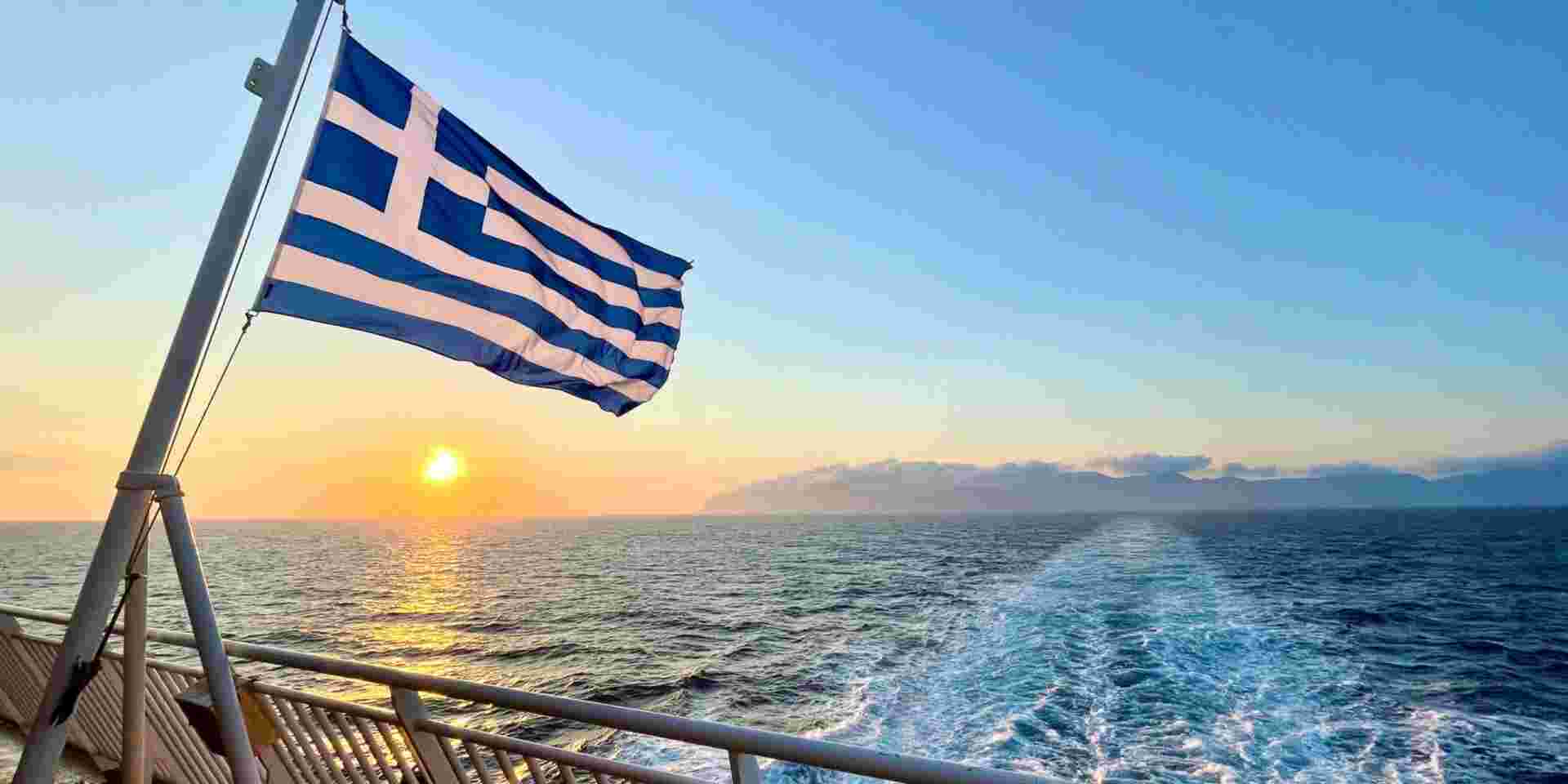 Greek flag and sunset view from the ferry between Greek islands in Naxos, Greece Greek Ferries_feature