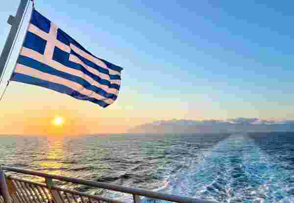 Greek flag and sunset view from the ferry between Greek islands in Naxos, Greece Greek Ferries_feature