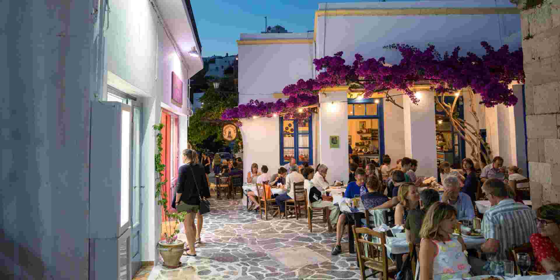 Milos island, Greece - June 11, 2018: Sunset scene in Plaka village which is full of shops and restaurants. People are dining in one of the restaurants decorated with bougainvillea flowers. milos_weather in greece in october_feature