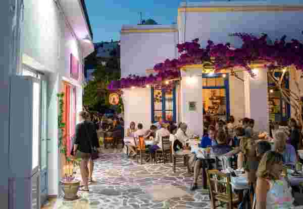Milos island, Greece - June 11, 2018: Sunset scene in Plaka village which is full of shops and restaurants. People are dining in one of the restaurants decorated with bougainvillea flowers. milos_weather in greece in october_feature