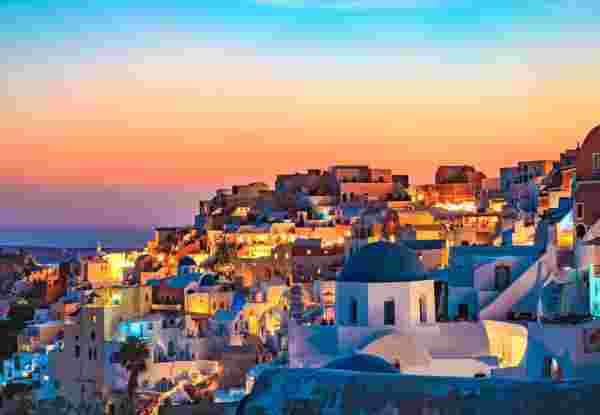 A picturesque view of Santorini at sunset, with whitewashed buildings and blue domes illuminated against a colorful sky. santorini sunset_romantic things to do in greece