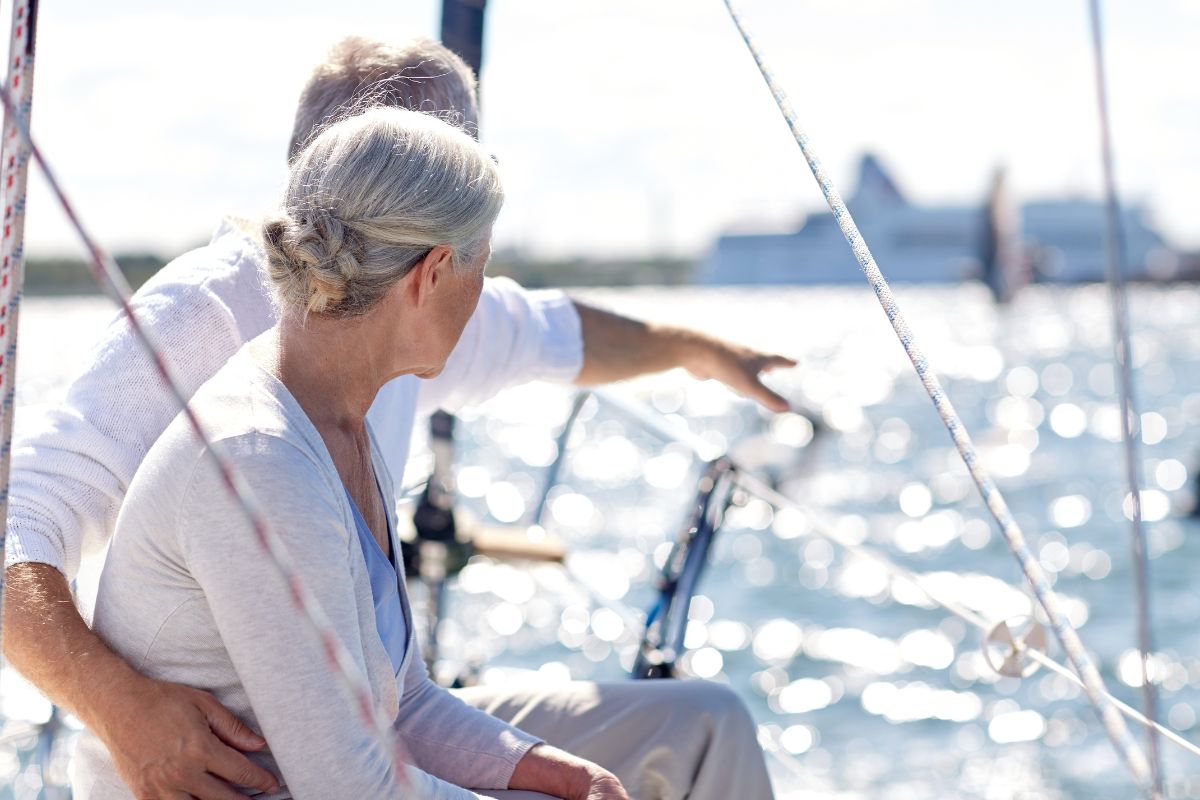 A senior couple on a ferry, with the man pointing towards the horizon, enjoying their travel on the water.