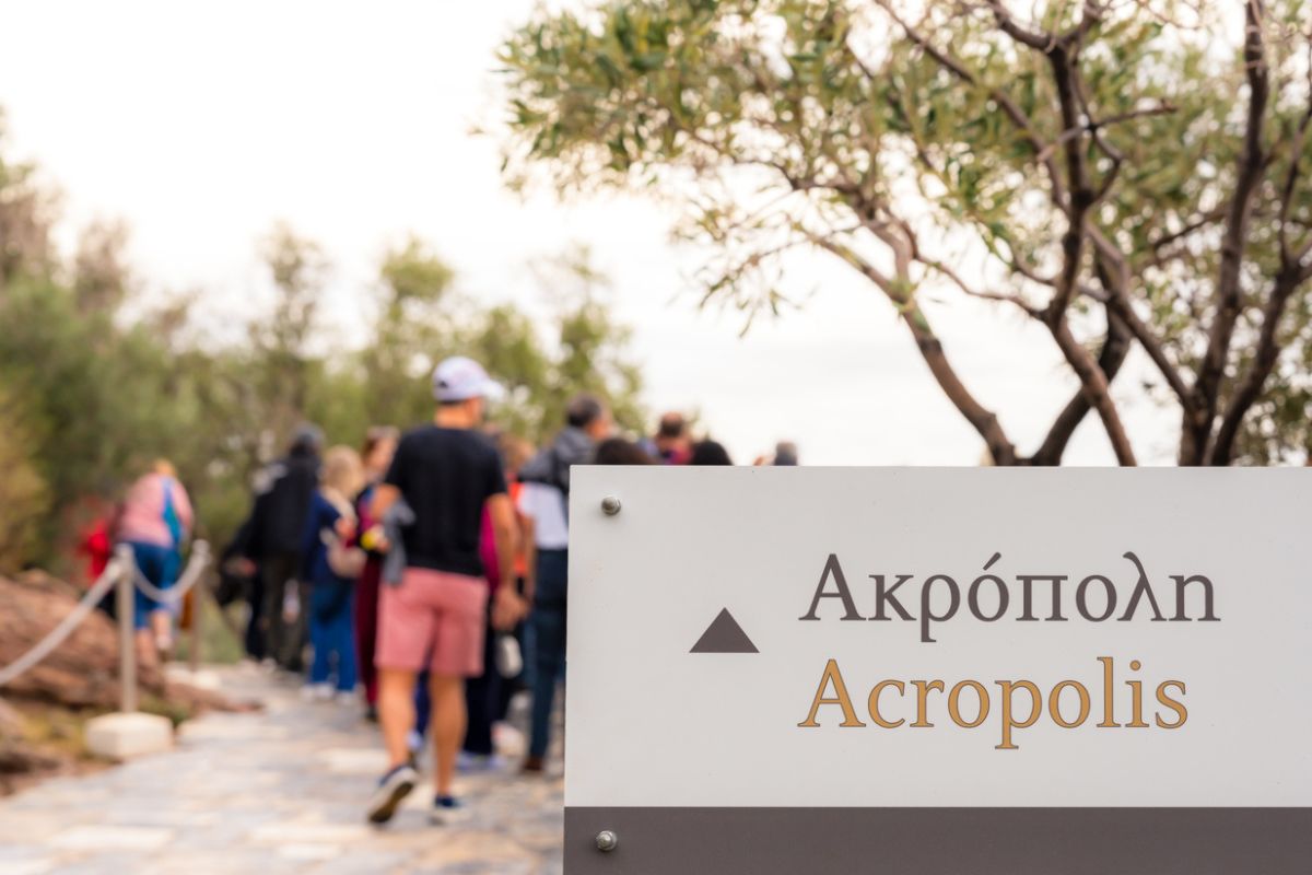 Close up on a sign with the word Acropolis in Greek and English on an information sign for tourists, with people, defocused in the background.