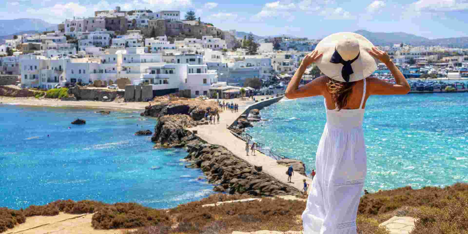 A solo female traveler in Naxos looks out over the sea and white buildings while holding her sunhat. Discover Greece Solo Travel Your Ultimate Guide_feature