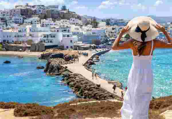 A solo female traveler in Naxos looks out over the sea and white buildings while holding her sunhat. Discover Greece Solo Travel Your Ultimate Guide_feature