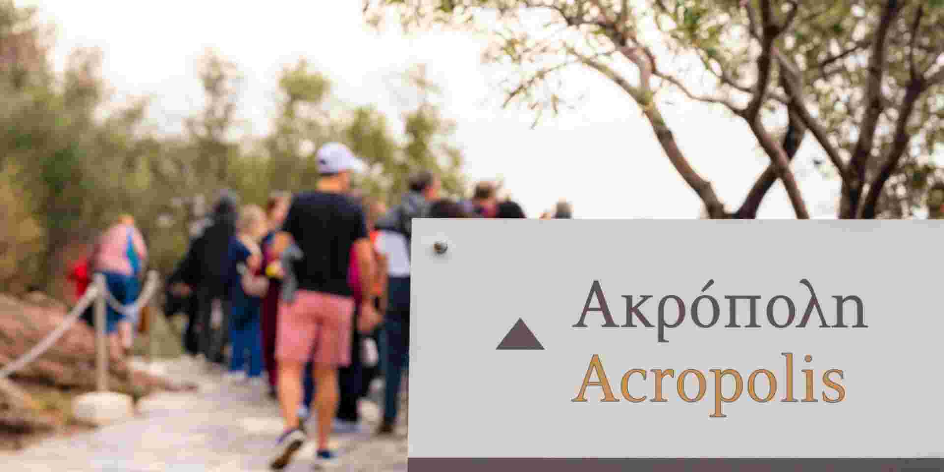 Close up on a sign with the word Acropolis in Greek and English on an information sign for tourists, with people, defocused in the background. Do They Speak English in Greece_feature