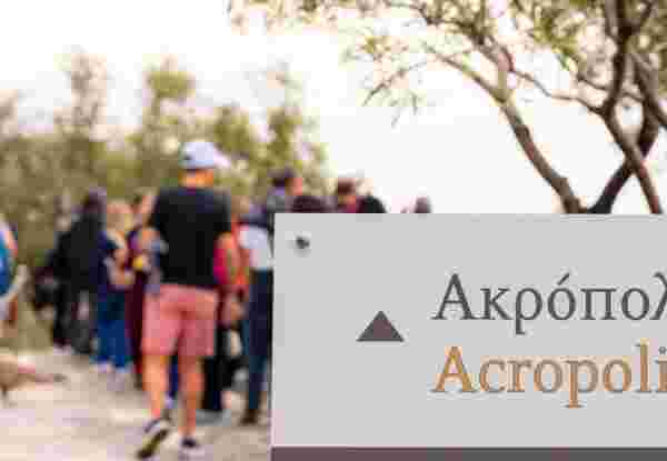 Close up on a sign with the word Acropolis in Greek and English on an information sign for tourists, with people, defocused in the background. Do They Speak English in Greece_feature