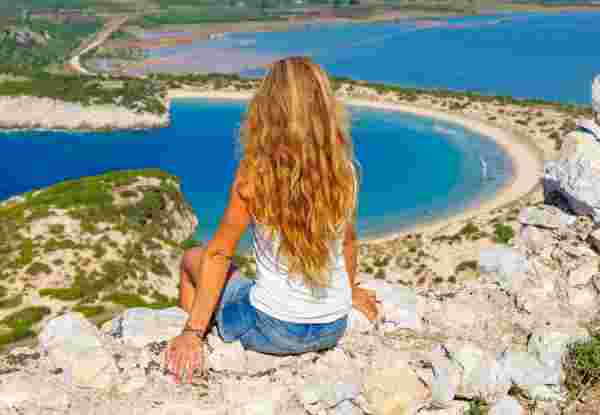 Beautiful Woman Admiring a Stunning Beach in Greece - Travel & Adventure best greek island for solo travel greece_feature