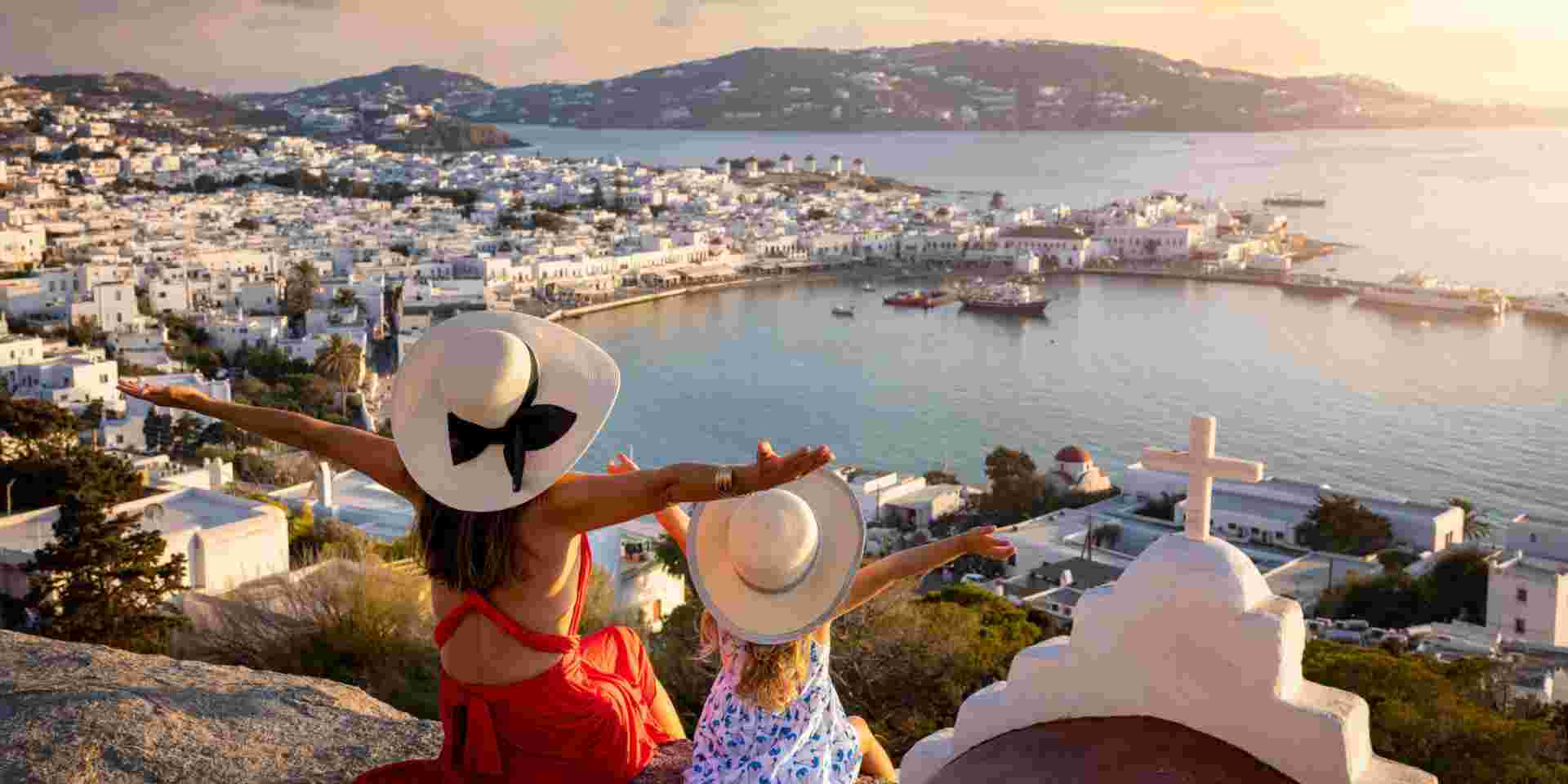 A happy mother and daughter on family holidays overlook the town of Mykonos island during a summer sunset, Cyclades, Greece best place to go in greece for families_feature