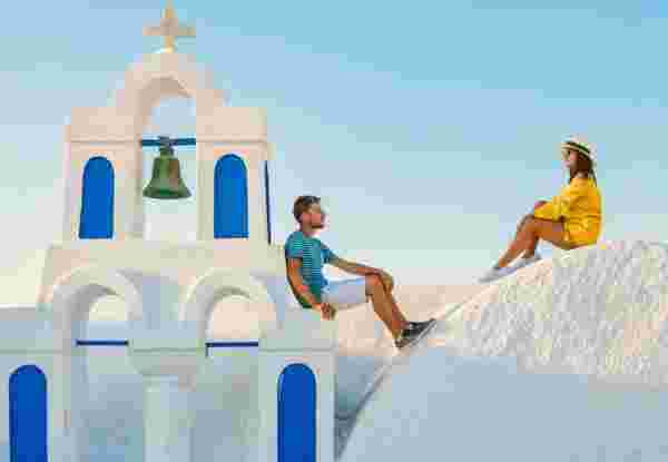 Young couple of men and women tourists visit Oia Santorini Greece on a sunny day during summer with whitewashed homes and churches, Greek Island Aegean Cyclades santorini couple_luxury honemoon in greece_feature