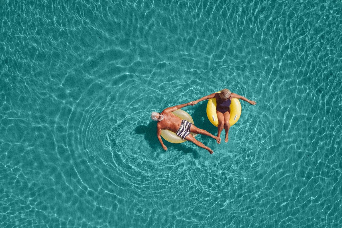 High angle view photo of a senior couple floating in the ocean while using swimming and floating devices