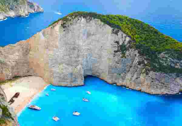 Yachts & pleasure boats moored in the turquoise waters just off Shipwreck Beach of Zakynthos. To the locals it's known as Navagio Beach. Stranded on the sand is the wreck of the Panagiotis (originally built in Scotland in 1937, and called the Saint Bedan), wrecked in 1980 and possibly engaged in nefarious, smuggler-type activities. Zakynthos Navagio_Where to go in Greece for first time_feature