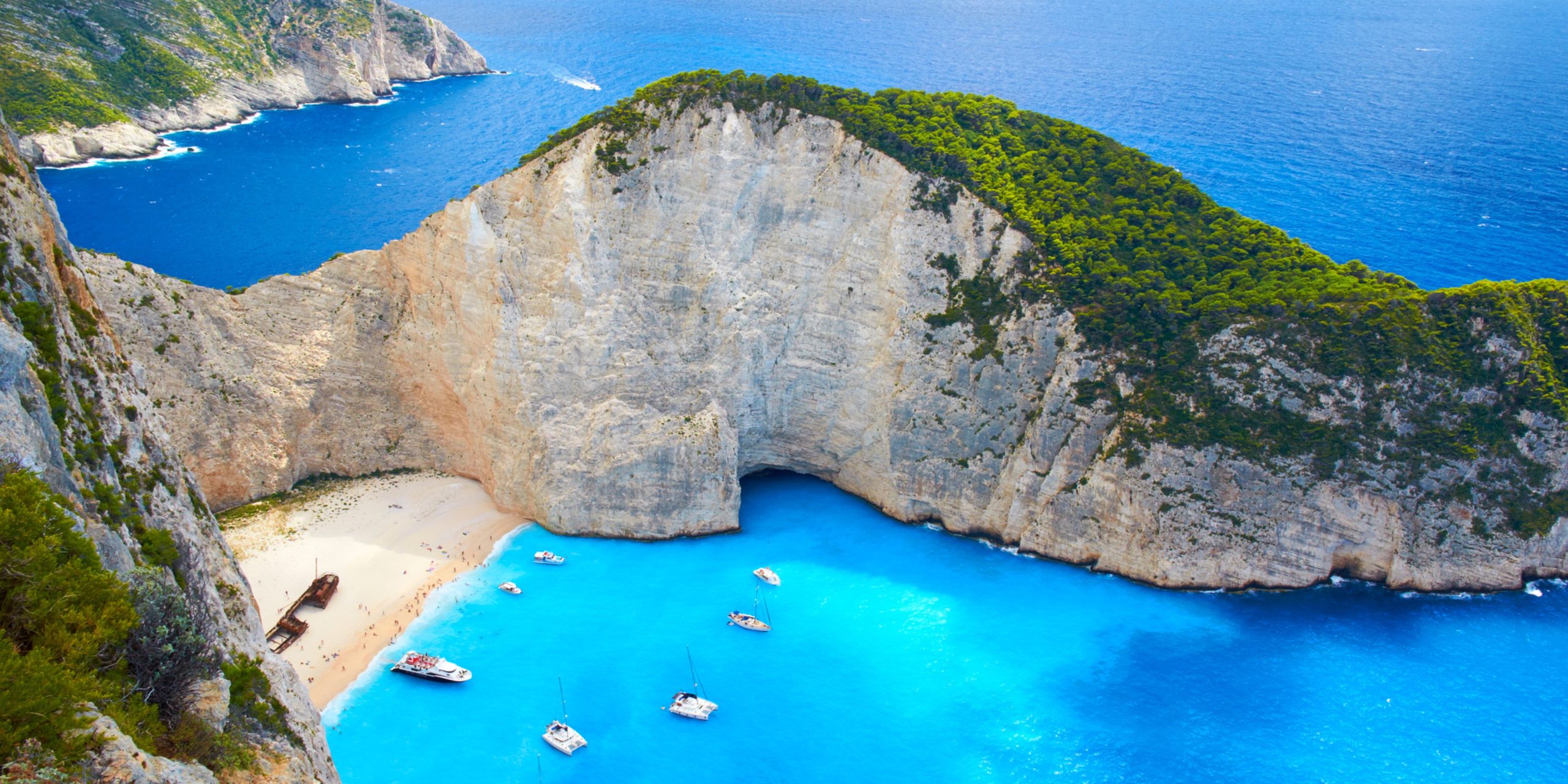 Yachts & pleasure boats moored in the turquoise waters just off Shipwreck Beach of Zakynthos. To the locals it's known as Navagio Beach. Stranded on the sand is the wreck of the Panagiotis (originally built in Scotland in 1937, and called the Saint Bedan), wrecked in 1980 and possibly engaged in nefarious, smuggler-type activities.