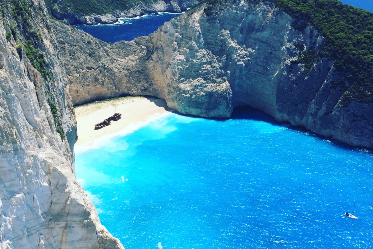 A view of Navagio Beach in Zakynthos, featuring a shipwreck on the sandy shore, surrounded by steep cliffs and vibrant blue waters.