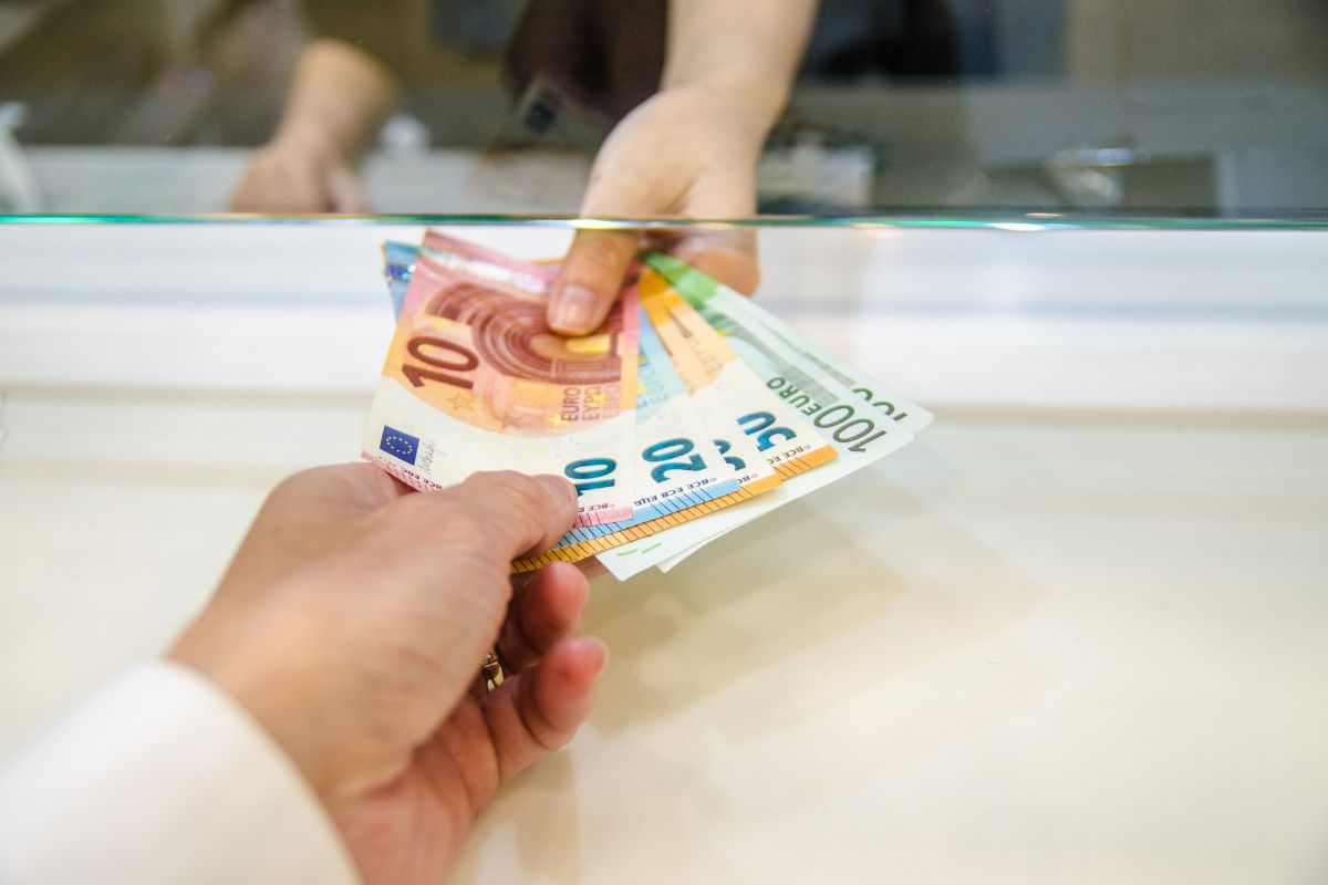 Person receiving Euro banknotes at a currency exchange counter, highlighting travel money preparation and foreign exchange services.