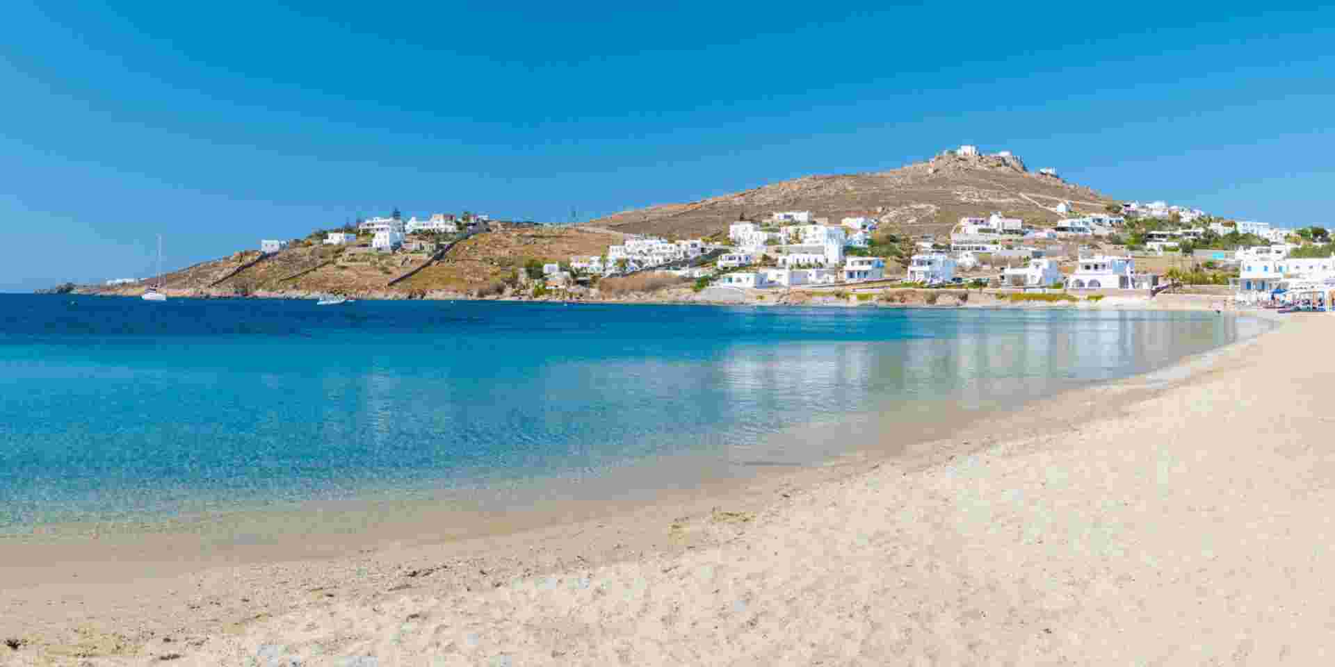Mykonos beach during summer with umbrella and luxury beach chairs beds, blue ocean with the mountain at Elia beach Mikonos Greece. elia beach mykonos_nudist beaches in greece_feature