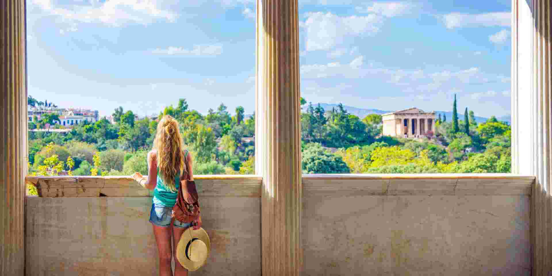 Woman tourist looking at Temple of Hephaestus, Athens in Greece- Ancient Agora temple of hephaistus in athens_traveling from crete to athens_feature