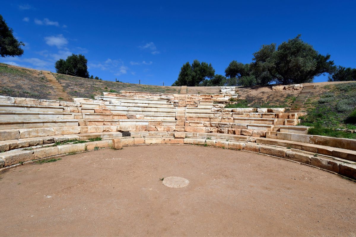 Ancient theater at the Aptera archaeological site in Chania, Crete, with stone seating under a clear blue sky.