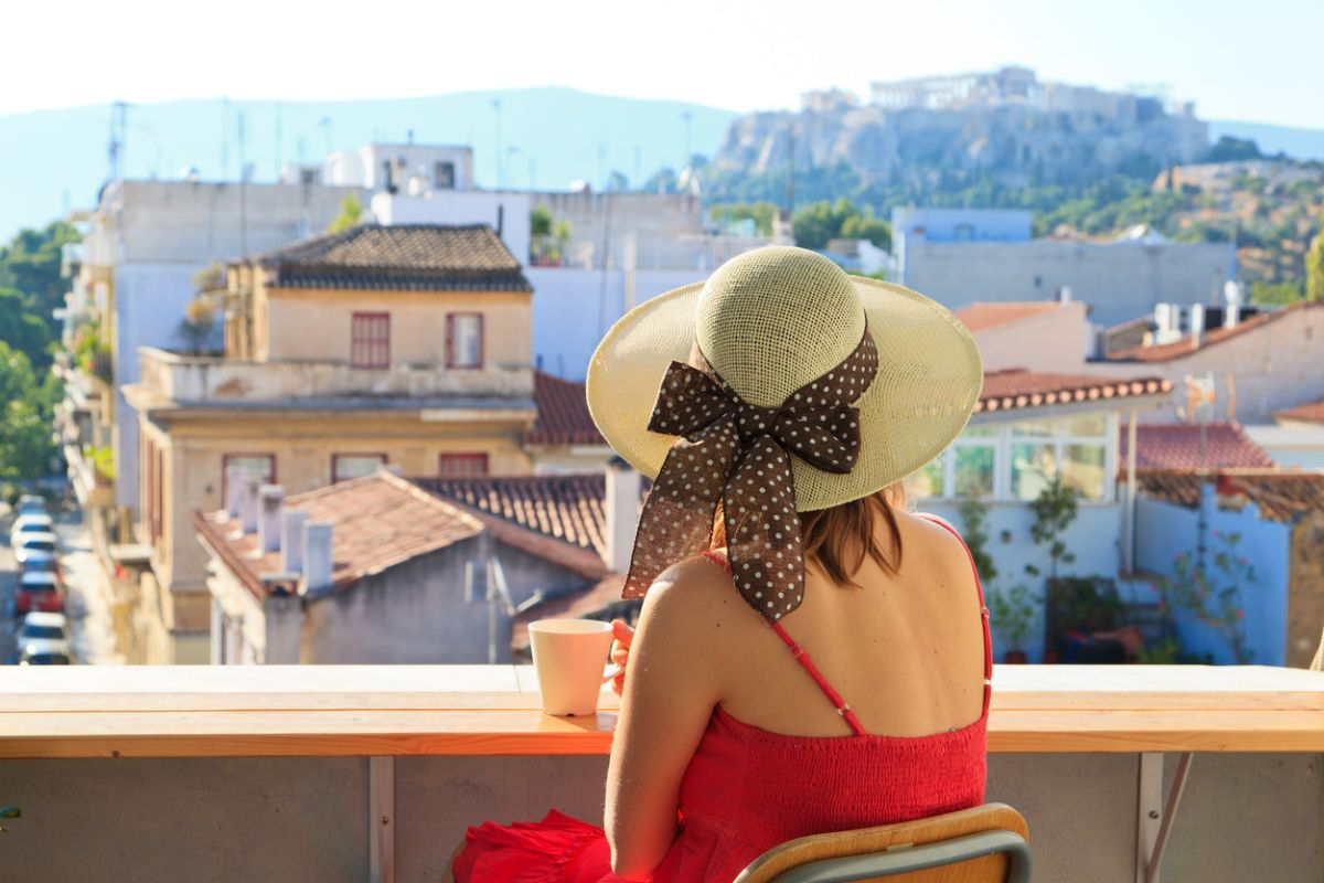 young woman with cup of coffee looking at Acropolis, travel concept_Weather in Italy and Greece in September