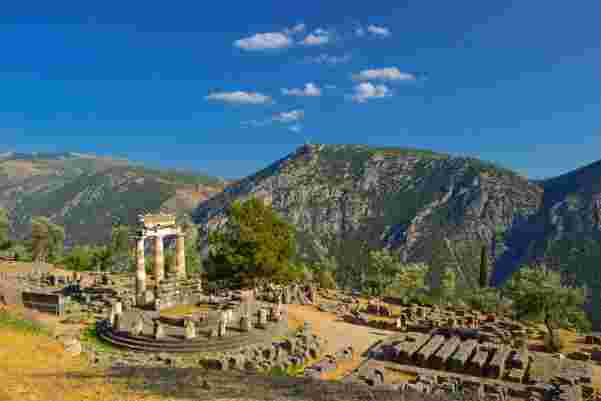 The Temple of Apollo in Delphi, Greece, with ancient ruins set against a backdrop of towering mountains and a clear blue sky. Delphi_temple of apollo