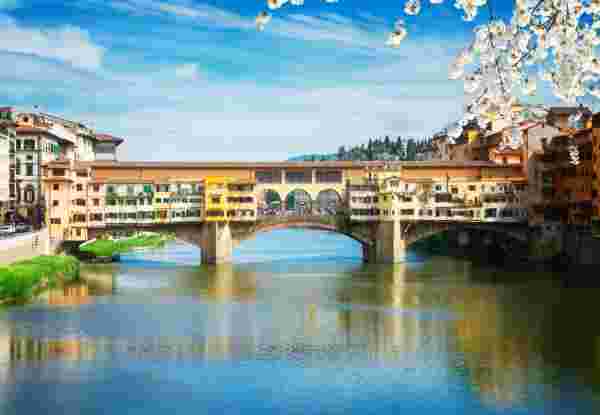 A view of Ponte Vecchio in Florence, Italy, with colorful buildings on the historic bridge reflected in the Arno River. Florence Italy