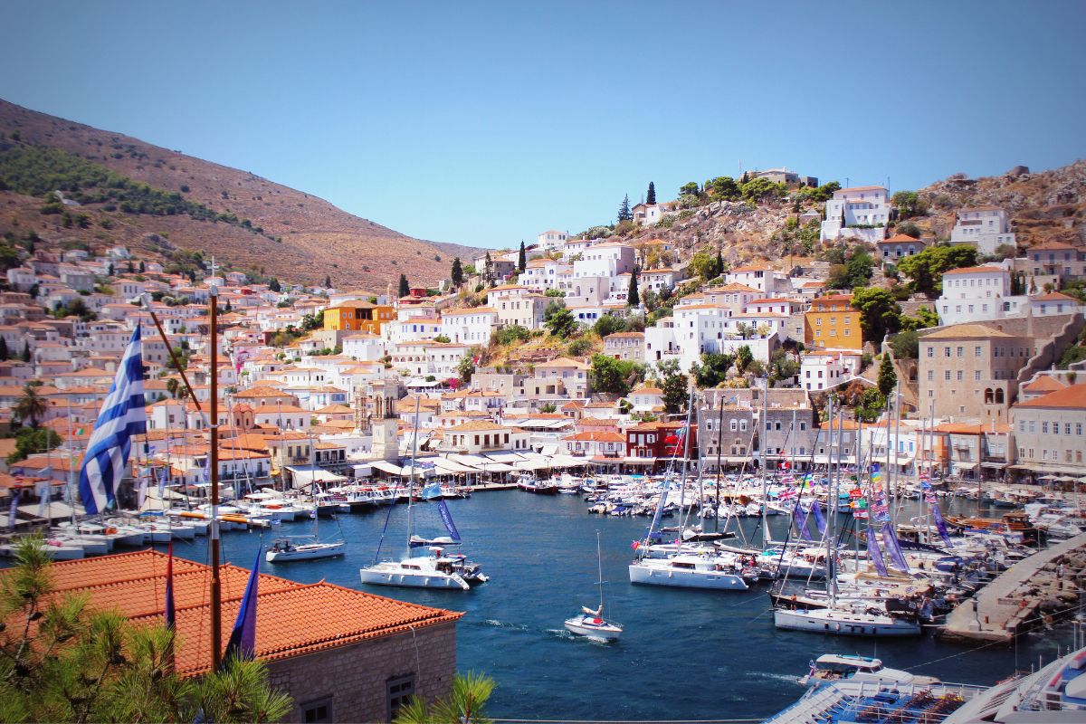 A view of Hydra Island, featuring a harbor filled with sailboats and yachts, surrounded by white and pastel-colored hillside building