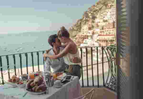 A couple enjoying breakfast on a balcony overlooking the sea and a hillside town in Italy during their honeymoon. Italy and Greece honeymoon_feature