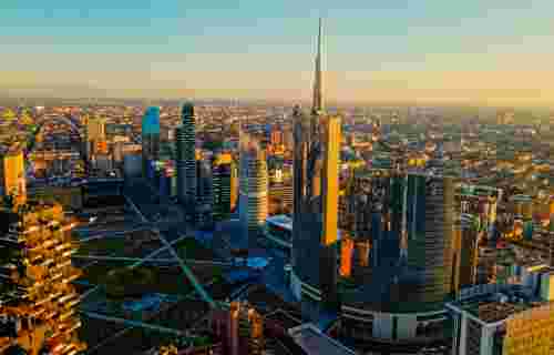 A picturesque aerial view of Milan with the sun setting, highlighting diverse architecture that juxtaposes traditional and contemporary styles. Golden Hour Over Milan's Modern Skyline