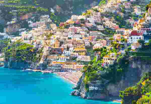 A view of Positano, Italy, with colorful hillside buildings overlooking the blue sea and a beach along the coastline. Positano_italy and greece itinerary 10 days_feature