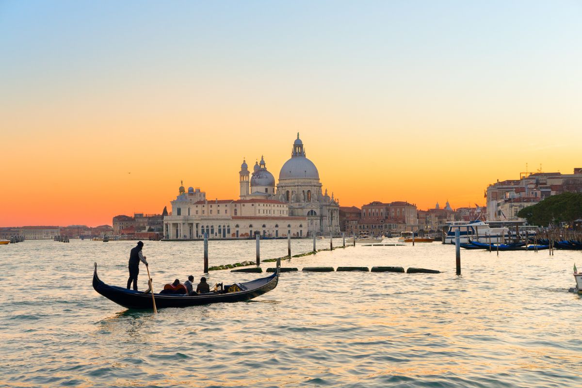 A gondola glides through the canals of Venice, Italy, at sunset, with the historic Basilica di Santa Maria della Salute in the background_Italy and Greece 14 Days of Adventure