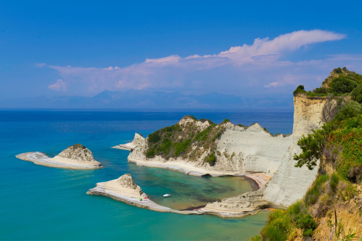 A coastal view of Corfu, Greece, featuring rocky white cliffs, small sandy inlets, and turquoise waters.