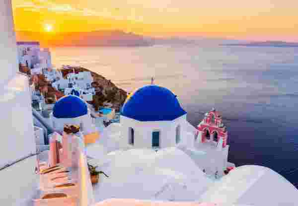 A picturesque view of Santorini, Greece, with white-washed buildings, blue-domed churches, and a golden sunset over the Aegean Sea. santorini