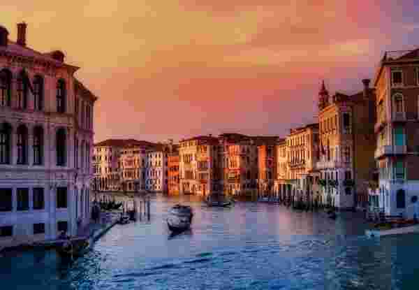 A beautiful view of Venice, Italy, at sunset, with gondolas gliding through the Grand Canal and historic buildings reflecting the warm evening light. venice_italy