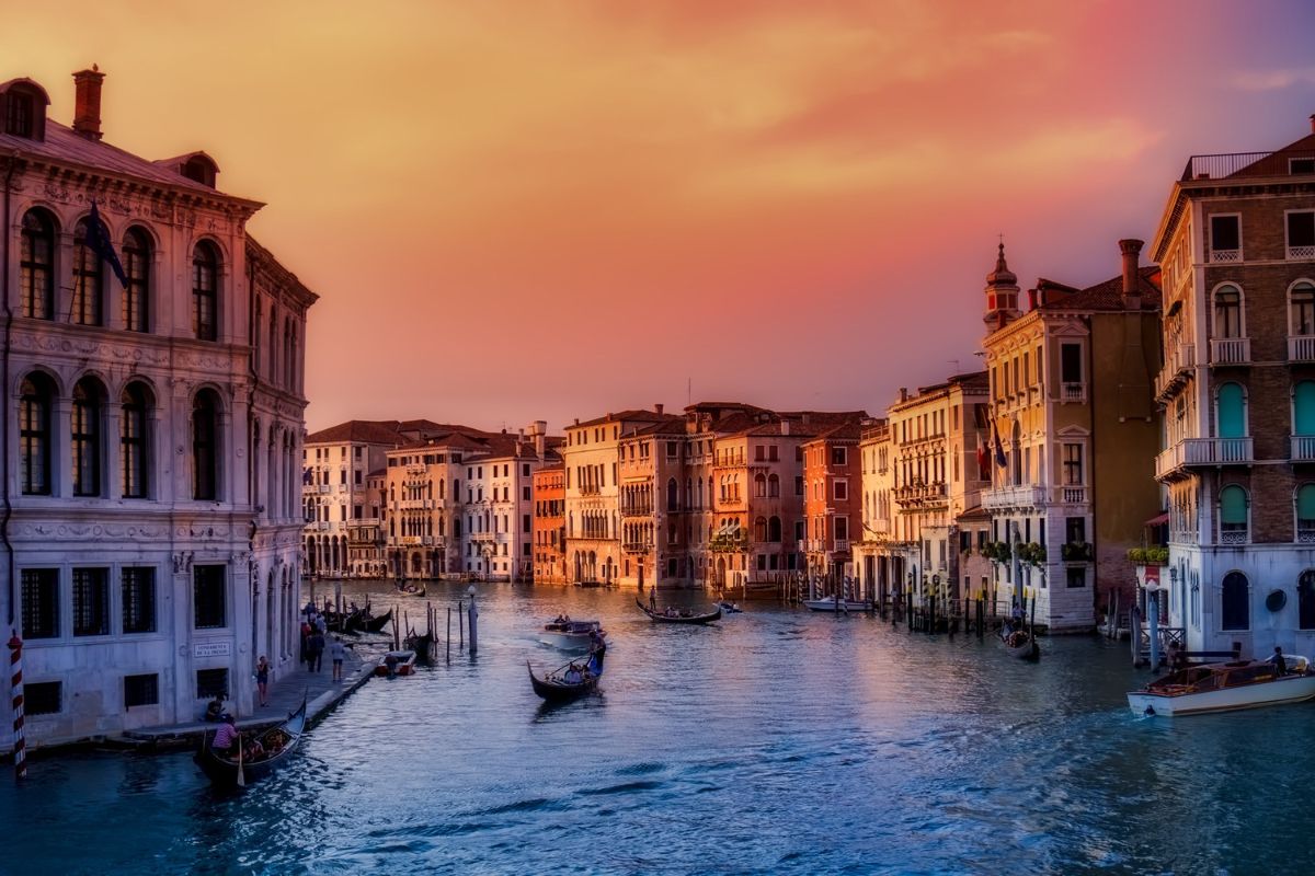 A beautiful view of Venice, Italy, at sunset, with gondolas gliding through the Grand Canal and historic buildings reflecting the warm evening light._Planning a Trip to Italy and Greece