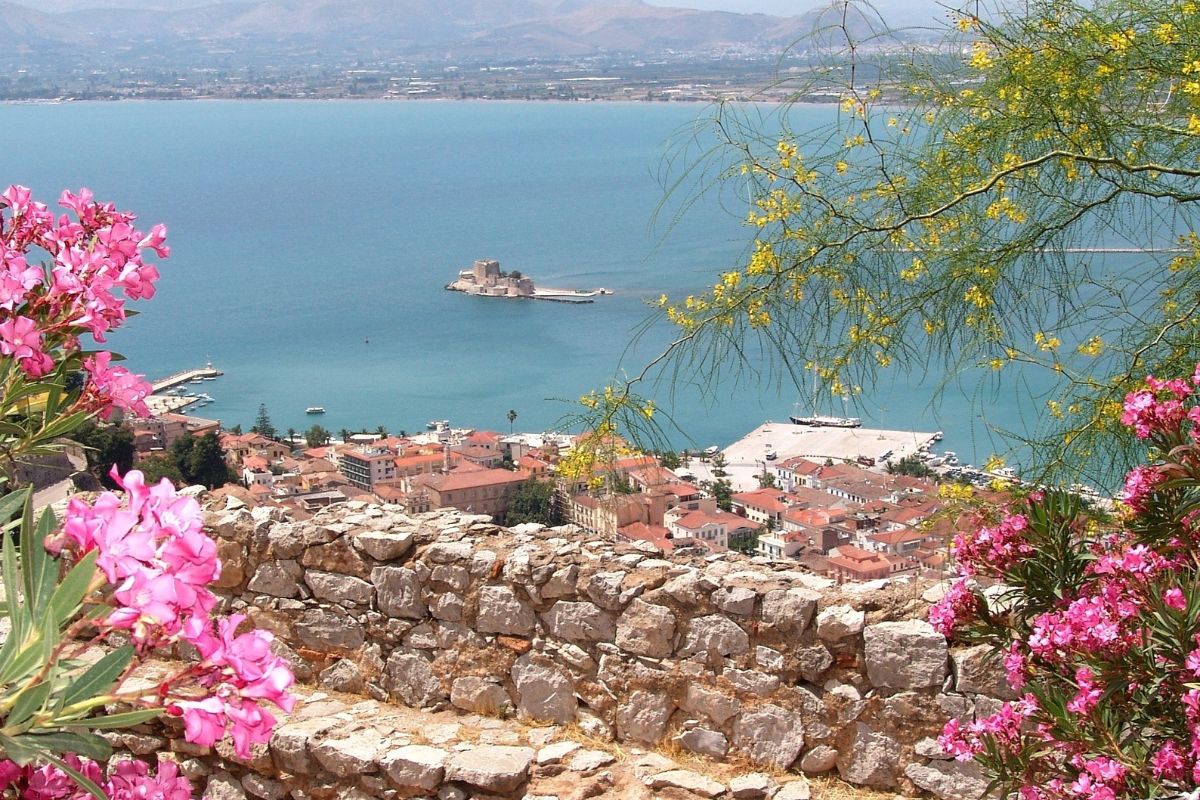 Scenic view of Nafplio, Greece in October with coastal town, sea fortress, and colorful flowers overlooking the harbor.