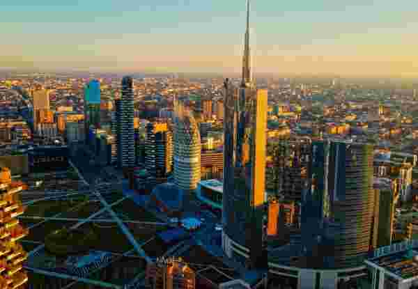 A picturesque aerial view of Milan with the sun setting, highlighting diverse architecture that juxtaposes traditional and contemporary styles. Milan_Feature