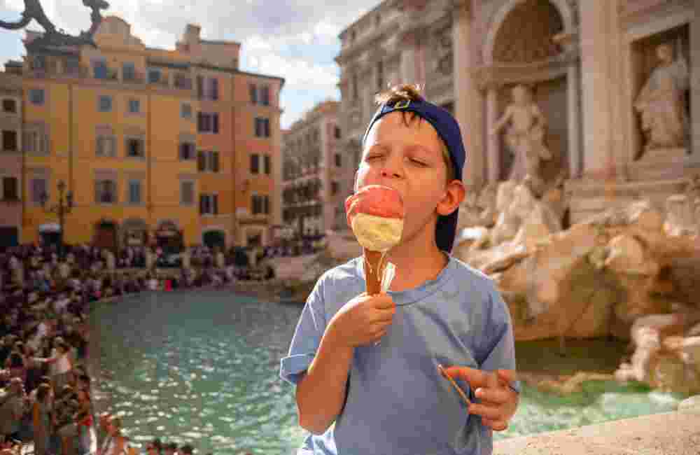 Cute cheerful boy 7 years old eating ice cream (gelato) near the Trevi Fountain in Rome, Italy.