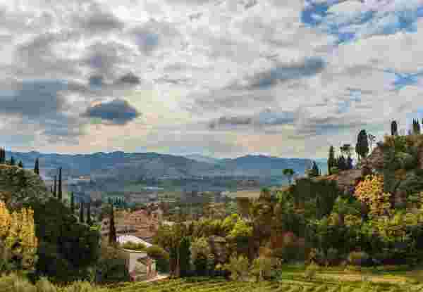 Scenic view of the Italian countryside with hills, vineyards, and a medieval castle under a partly cloudy October sky. weather in italy in october_feature