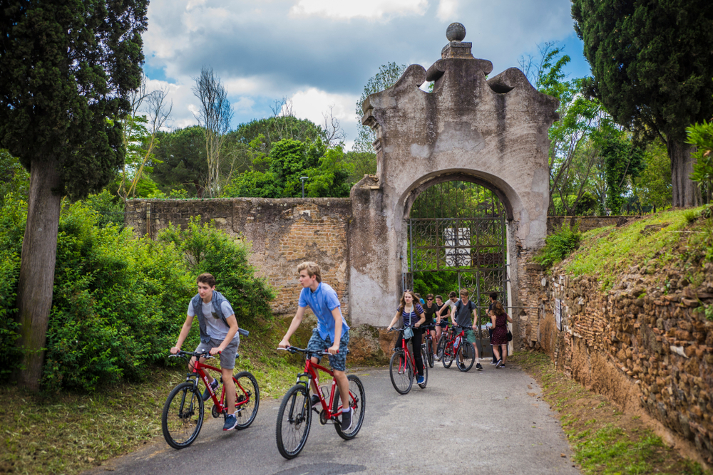 Teenagers cycling along the Appian Way near ancient Roman ruins during an outdoor adventure in Rome