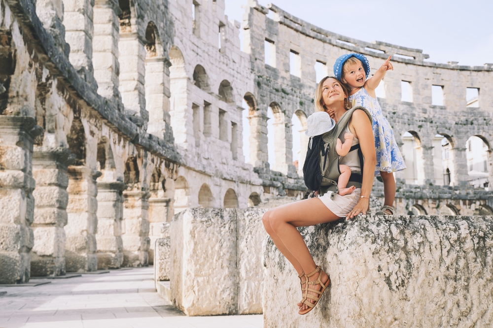 Mother travelling with two young children inside an ancient Roman amphitheatre