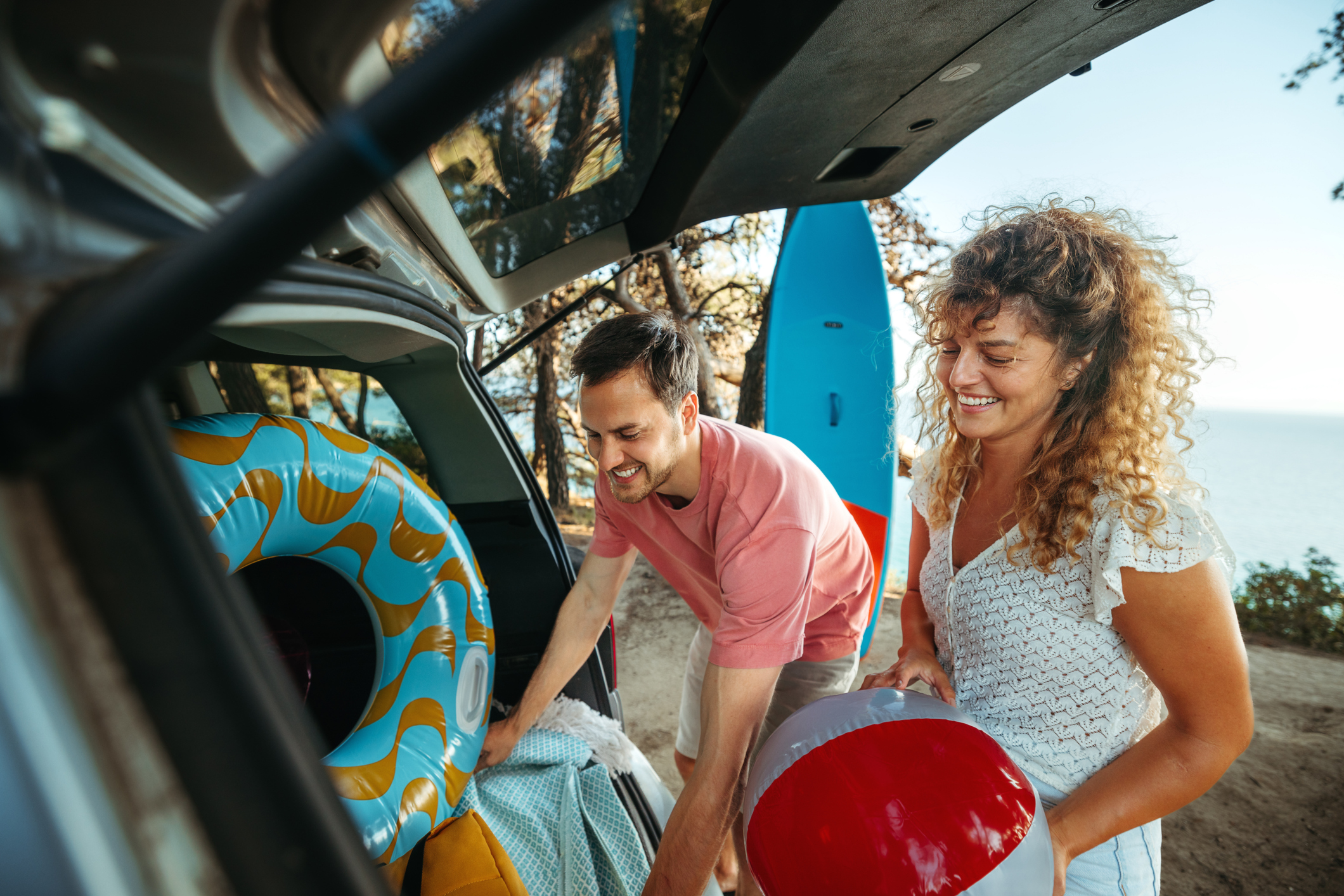 Young couple unpacking car trunk while getting ready for the beach adventure
