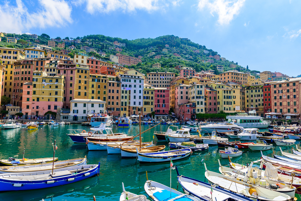 Colourful waterfront buildings and fishing boats in Camogli harbour on the Italian Riviera under a bright blue sky