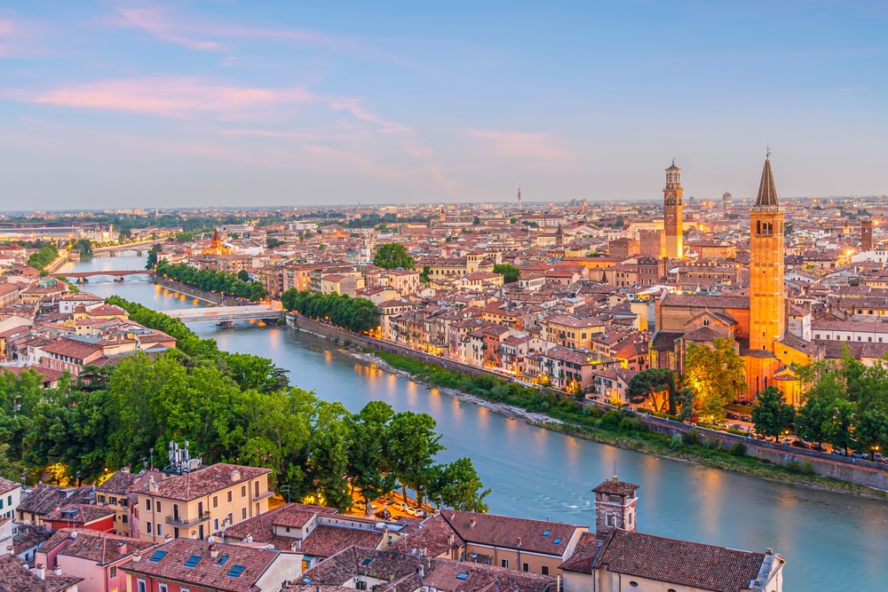 Panoramic view of Verona and the Adige River at dusk with illuminated historic buildings and church towers