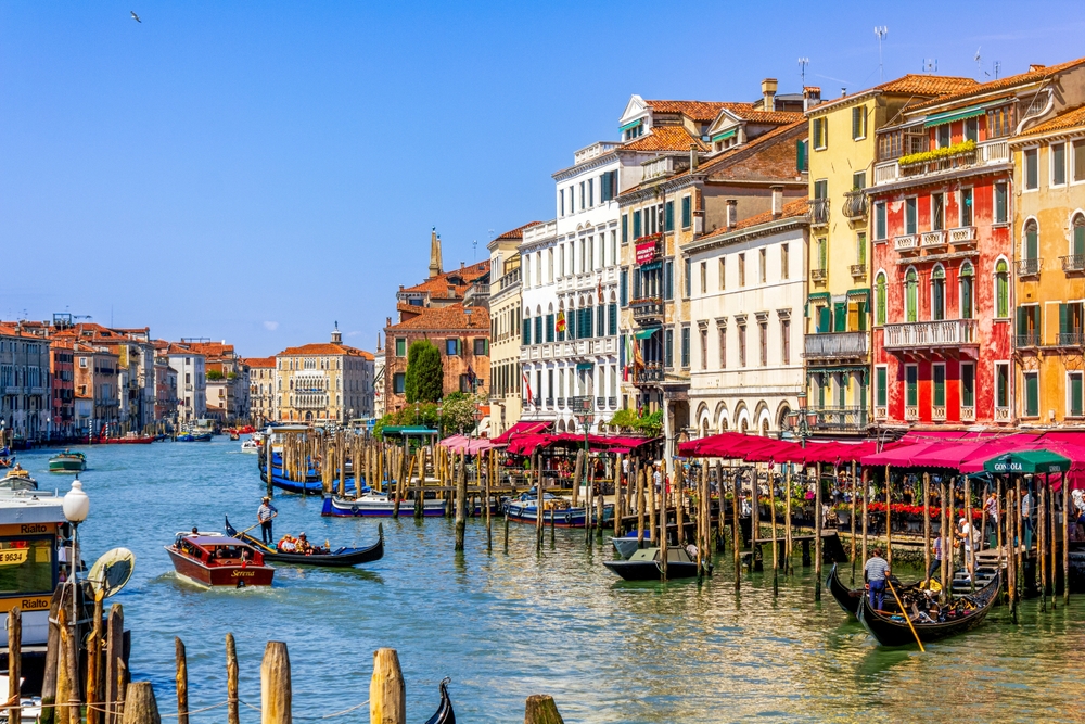 Grand Canal in Venice lined with colorful historic buildings, gondolas and boats under a clear blue sky