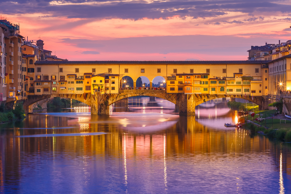 Ponte Vecchio in Florence glowing at sunset with reflections across the Arno River