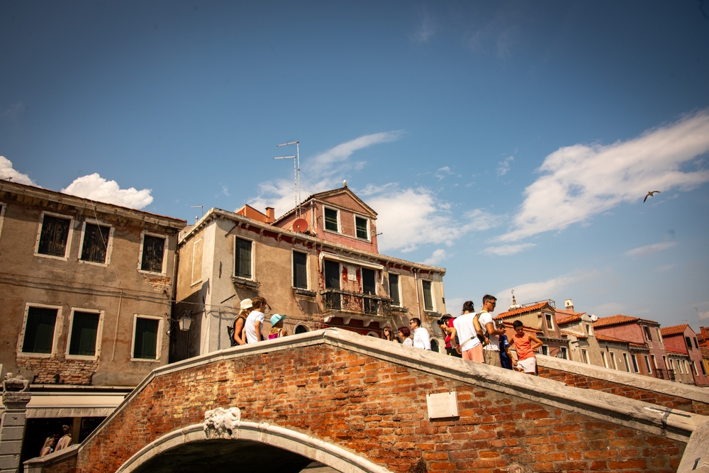 Visitors crossing a traditional brick bridge in Venice surrounded by historic buildings and canals 