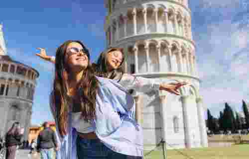 Mother and daughter posing playfully in front of the Leaning Tower of Pisa on a sunny day in Tuscany